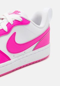 Vita sneakers med en rosa läder Swoosh och detaljer, strukturerad syntetisk ovandel och en vit gummisula med färgade fläckar.