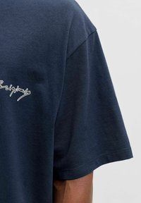 Marineblå bomulls-t-skjorte med en avslappet passform. Har rund hals og korte ermer. Hvitt logo med skriftstilhøyde på fronten.