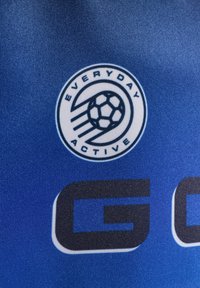 Blått tyg med en cirkulär logotyp som har en fotboll och texten "EVERYDAY ACTIVE." Tydlig bokstav "G" också synlig.