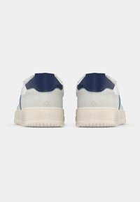 Bílé a modré tenisky s hladkým koženým svrškem, strukturovanými semišovými detaily a krémovou gumovou podrážkou. Minimalistický design s zaoblenými hranami.