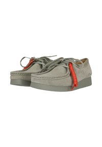 Chaussures en suede gris avec un bout arrondi, semelle en caoutchouc et détail en lacets orange décoratifs en boucle. Texture douce avec des accents cousus.
