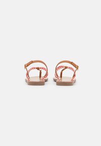 Brown leather sandals with braided coral straps, flat sole, and adjustable ankle buckle. Minimalist design, open back, and casual aesthetic.