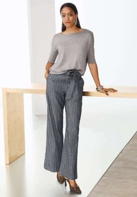 Grauer Strickoberteil mit Nieten, kombiniert mit navyblauen, gestreiften, weit geschnittenen Hosen mit einem Bindegürtel. Braune gemusterte Absatzschuhe und silberne Accessoires runden den Look ab.