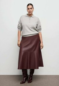 Svijetlosivi pamučni džemper s ovratnikom, uparen s midi suknjom od vinsko crvene kože i čizmama do koljena u istoj boji. Glatke teksture i krojena odjeća.