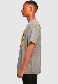 Graues Baumwoll-T-Shirt mit lässiger Passform und überschnittenen Schultern. Auf der Vorderseite befindet sich ein grafischer Druck in Rot und Gelb.