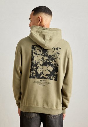 Olive green hoodie with a drawstring hood. Features a black and white graphic on the back with text and a textured finish.