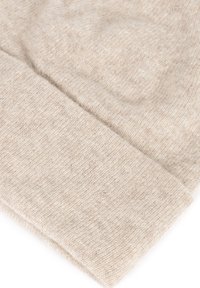 Beżowa dzianina o miękkiej, fakturowanej powierzchni. Materiał przedstawia delikatny wzór, z zagiętymi krawędziami zapewniającymi schludne wykończenie.