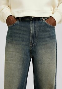 Tummanpesun farkut haalistuneella gradientilla, klassisella viiden taskun mallilla ja näkyvillä ompelusaumoilla.