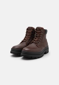 Botas de cuero marrón con punta redonda, costuras reforzadas, diseño de cordones y suelas de goma negra con un patrón texturizado.