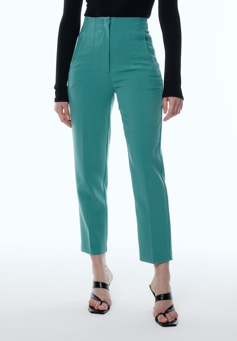 Tegengeschiedenis hoge taille broek in teal met een gladde textuur, recht gesneden ontwerp en voorplooien. Draagt met zwarte strappy hakken.