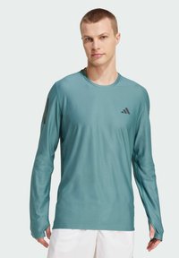 Langärmliges Sportshirt in Türkis, aus feuchtigkeitsableitendem Stoff, mit einem dezenten Logo auf der Brust und Daumenlöchern in den Bündchen.