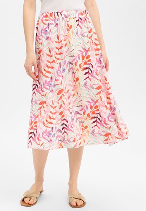 Vrouw draagt een midirok met kleurrijke bloemen- en bladranden in roze, oranje, paars en lichtblauw, gecombineerd met beige sandalen met open tenen.