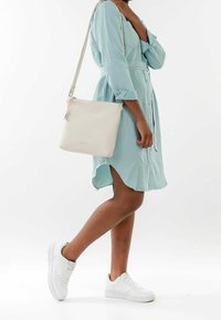 Borsa a tracolla in pelle bianca con texture liscia e design minimalista, dotata di una cerniera argentata e tracolla regolabile.