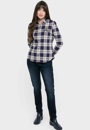 Camisa de botones de cuadros en azul marino con patrones en gris, blanco y burdeos; forma ajustada. Combinada con jeans de mezclilla oscuros y botas de goma.