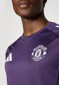 Lilla sportsjersey med Manchester United-logo i hvid. Lavet af glat stof med rund hals og hvide side-striber.
