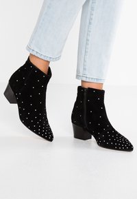 Schwarze Wildleder-Stiefeletten mit spitzen Zehen, ausgestattet mit silbernen Nietenverzierungen, niedrigen Blockabsätzen und seitlichen Reißverschlüssen für einfaches Anziehen.