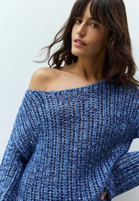 Maglione blu lavorato a maglia off-the-shoulder con lavorazione aperta, maniche lunghe e vestibilità rilassata. Presenta un design leggero e testurizzato.