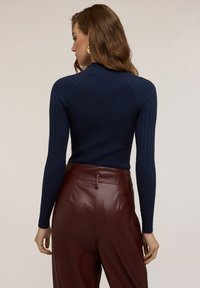 Maglione a collo alto a coste di colore blu navy con maniche lunghe, abbinato a pantaloni in pelle marrone a vita alta, mostra la vista posteriore e i dettagli della cucitura della spalla.