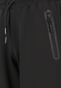 Svarta joggers med ett elastiskt midjeband, dragsnören och en sidoficka med dragkedja för säker förvaring. Slät, mjuk tygkänsla.