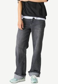 Graue Denim-Jeans mit lockerer Passform, aufgerollten Säumen und mittelhohem Bund. Getragen mit einem schwarzen Sweatshirt und mintgrünen Turnschuhen.