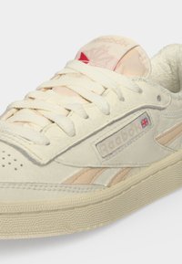 Ανοιχτό μπεζ αθλητικό παπούτσι Reebok με υφασμένα κορδόνια, διάτρητη μύτη και λογότυπο της Union Jack στην πλευρά κοντά στο όνομα της μάρκας.