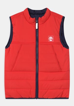 Gilet imbottito rosso senza maniche con cerniera frontale, bordo blu navy e logo bianco sulla parte superiore sinistra del petto.