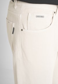 Acercamiento de pantalones de color crema que muestran los bolsillos delanteros y de moneda con una pequeña etiqueta metálica "Antony Morato" sobre el bolsillo.