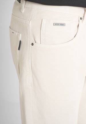 Acercamiento de pantalones de color crema que muestran los bolsillos delanteros y de moneda con una pequeña etiqueta metálica "Antony Morato" sobre el bolsillo.