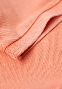 Koraalstof met een gestructureerde weving, met een gevouwen rand. Het oppervlak is soepel met subtiele kleur- en lichtreflectievariaties.