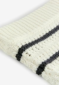Texturerad, stickad filt i krämfärg med mörkgrå ränder. Har ett vävt mönster och mjukt, tjockt garn för värme och komfort.