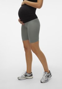 Zwangerschaps fietsshorts van zacht, rekbaar grijs materiaal, met een lengte tot de middel van de bovenbenen, gecombineerd met een zwart aangesloten top en zilveren hardloopschoenen.