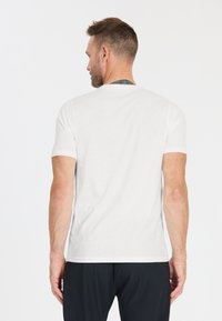 Biała bawełniana koszulka z krótkim rękawem, okrągłym dekoltem i prostym wzorem. Z tyłu widoczny tatuaż na górnej części ramienia.