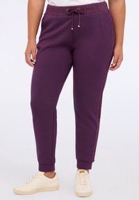 Lila Jogginghose mit einem glitzernden Bund, Kordelzug und seitlichen Akzenten. Hergestellt aus weichem Stoff mit gerippten Bündchen an den Knöcheln.
