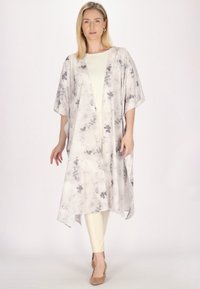 Kimono ușor, alb, cu modele florale gri. Are mâneci late și un design fluid, purtat peste un top crem și pantaloni bej.