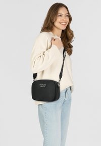 Svart crossbody-väska i slätt material, med rektangulär form, dragkedjestängning och tryckt logotyp på framsidan. Justerbart axelband.