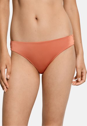 Kobieta ubrana w gładkie koralowe majtki od bikini, ukazująca środkową część ciała i górną część ud na jednolitym białym tle.