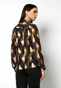 Langärmlige Bluse aus leichtem Material mit einem mehrfarbigen geometrischen Muster in Brauntönen, Senfgelb und Rosa, mit geknöpften Manschetten.