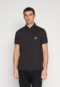 Polo nero in cotone, con colletto, maniche corte e un piccolo logo bianco sul lato sinistro del petto.