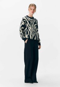 Schwarzer und cremefarbener, gestreifter Pullover mit Rundhalsausschnitt, kombiniert mit weiten schwarzen Hosen. Weicher Stoff, lässiges Design und überschnittene Schultern.