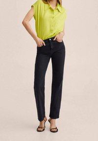 Blusa senza maniche verde lime con chiusura a bottone e tasca, abbinata a jeans neri a gamba dritta a vita alta e sandali neri con cinturini.