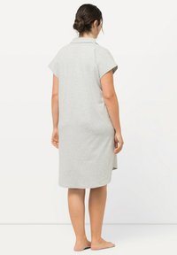 Vestido gris de manga corta con cuello, de textura suave, a la altura de la rodilla y con aberturas laterales para facilitar el movimiento. Visto desde la parte posterior.