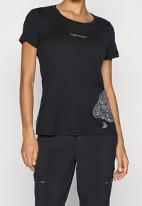 Czarna koszulka z krótkim rękawem i okrągłym dekoltem, z pomarańczowym logo oraz białym konturowym wzorem mapy na dole. Miękka w dotyku o luźnym kroju.