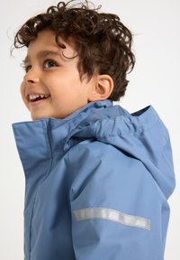 Lichtblauwe waterdichte jas met een capuchon, voorzien van een zilveren reflecterende streep op de mouw, gemaakt van glad, duurzaam materiaal.