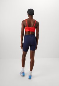 Rød Nike Pro sports-BH med justerbare stropper, kombinert med marineblå shorts. Har synlig merkevare og en tettsittende design.