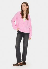 Rosa oversized kofta med V-ringning, med fem knappar och ribbstickade ärmslut, som bärs med mörka jeans och bruna loafers.