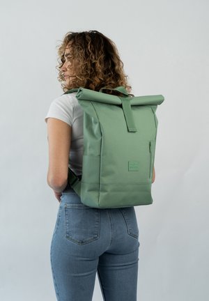 Sac à dos vert à rabat, fabriqué en tissu résistant, doté de bretelles ajustables, d'une poche zippée à l'avant et d'un insigne texturé.