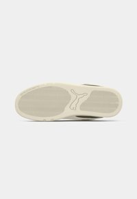 Shoe sole in cream rubber with textured grip patterns. Features a logo imprint and subtle wave design for enhanced traction.
