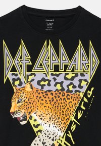 Czarna koszulka z logo zespołu „Def Leppard” nad ilustracją pomarańczowo-czarnej pantery oraz napisem „Hysteria” z boku.