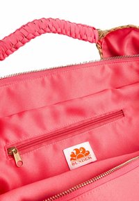 Borsa in tessuto corallo con manico intrecciato, dotata di una cerniera dorata e di una tasca interna con zip. Include un'etichetta con un logo raffigurante un sole.