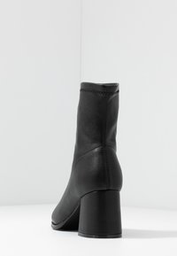 Bottines en cuir noir avec un talon carré, texture lisse, détails de coutures verticales et une coupe ajustée.